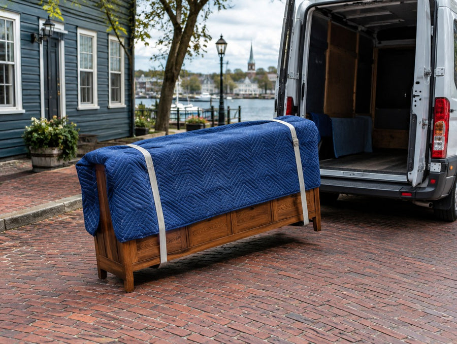 A blanket-wrapped console carried to a delivery van on a brick street in a New England river town